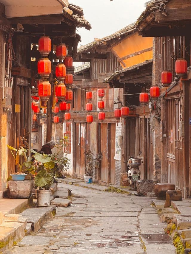 Fili di lanterne rosse pendono sopra uno stretto vicolo di pietra fiancheggiato da edifici tradizionali in legno.