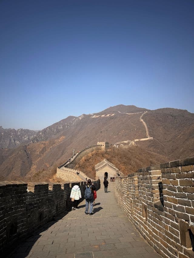 Un viaggio di gruppo WeRoad percorre un grande muro di pietra che si snoda attraverso montagne aride e ondulate sotto un cielo azzurro e limpido.