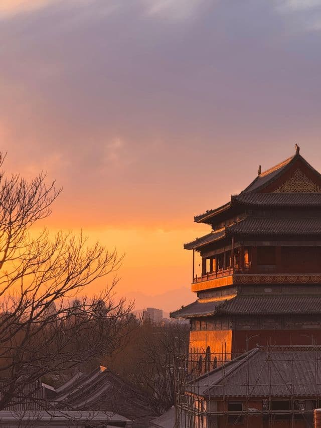 Una tradizionale pagoda a più piani è illuminata da un tramonto arancione, con alberi spogli in primo piano e uno skyline sullo sfondo.