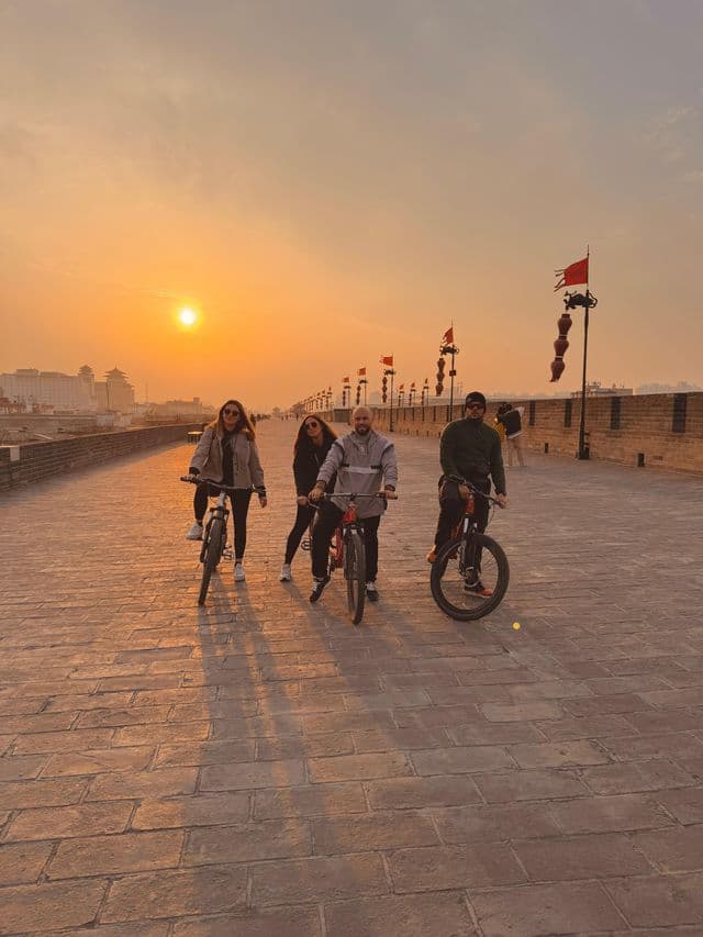 Un viaggio di gruppo WeRoad di quattro persone in bicicletta in posa su un'ampia cinta muraria acciottolata al tramonto.