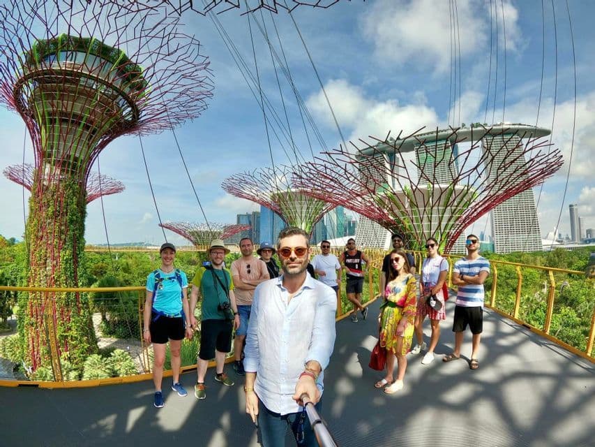 Un gruppo WeRoad si scatta un selfie su una passerella sospesa tra futuristici Supertrees con lo skyline della città sullo sfondo.