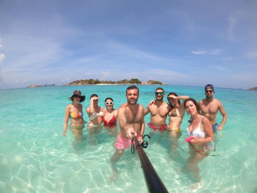 Un gruppo WeRoad si scatta un selfie con un'asta per selfie in acqua cristallina turchese, con isole tropicali sullo sfondo.