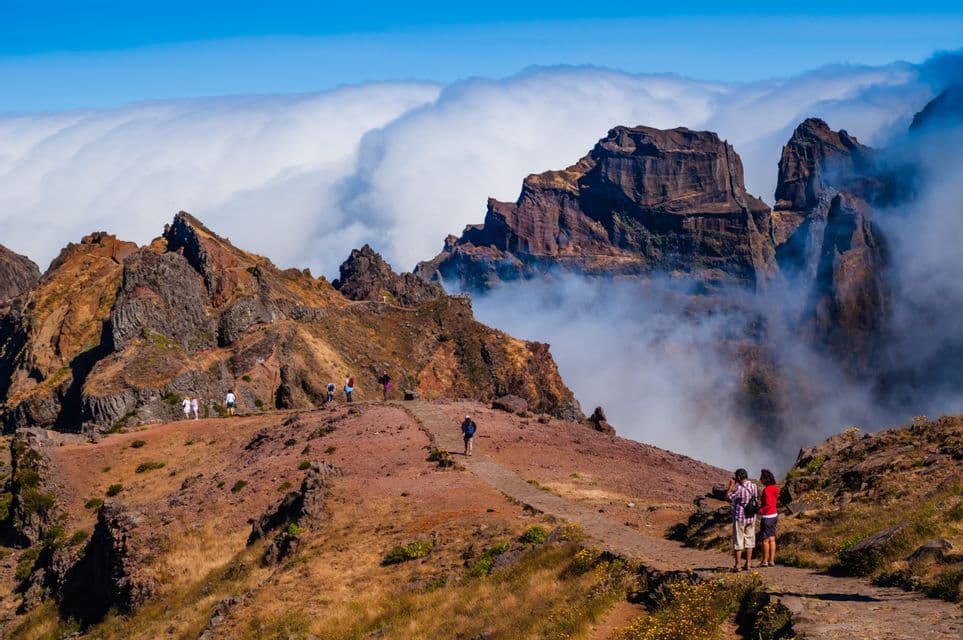 A WeRoad group trip hikes on a trail through rugged mountain peaks that rise above a sea of white clouds.