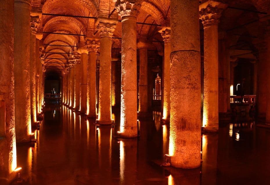 Una cisterna subterránea con filas de grandes columnas y techos abovedados, iluminada por luces cálidas que se reflejan en el agua.