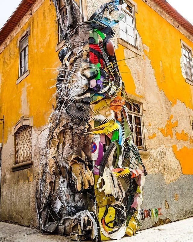 A large sculpture of a rabbit made from colorful recycled materials attached to the corner of a yellow building.
