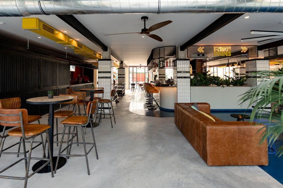 El interior vacío de un bar moderno de estilo industrial con mesas altas, taburetes de cuero marrón y un largo sofá de cuero.