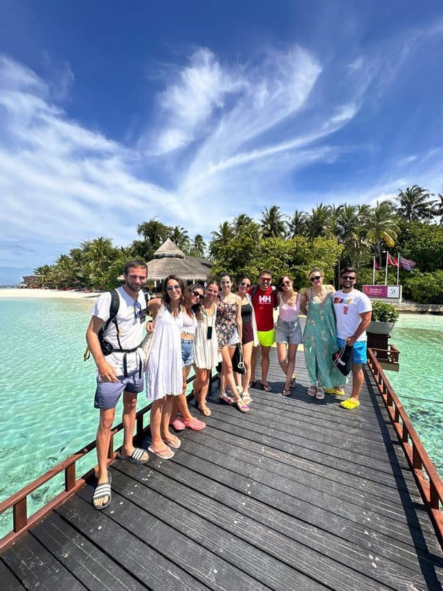 Un grupo de WeRoad posa para una foto en un muelle de madera sobre agua turquesa, con una isla de palmeras de fondo.