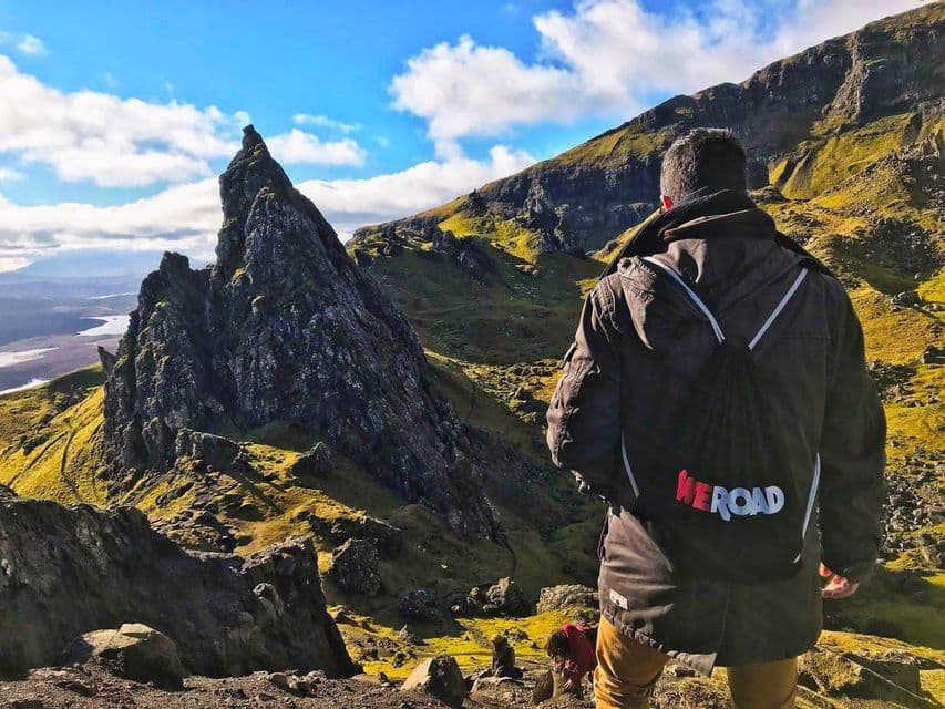 Un voyageur WeRoad, vu de dos, contemplant un paysage montagneux accidenté avec un piton rocheux proéminent.