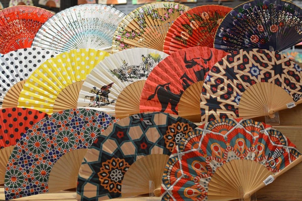 Una collezione di coloratissimi ventagli spagnoli con vari motivi come pois, forme geometriche e scene di corrida.