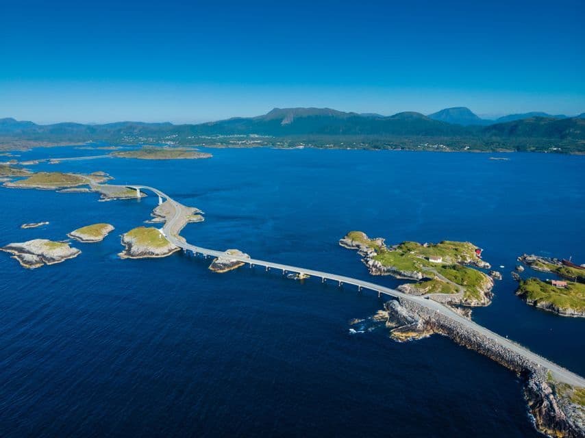 Una vista aérea de una carretera costera sinuosa que une varias islas pequeñas y rocosas en un mar azul profundo bajo un cielo despejado.