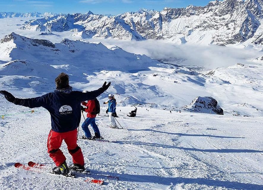 A WeRoad group trip skiing down a snowy slope with a panoramic view of snow-capped mountains.