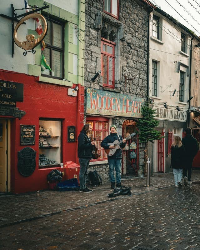 Deux musiciens jouent de la guitare et du violon dans une rue pavée mouillée devant des bâtiments historiques colorés.