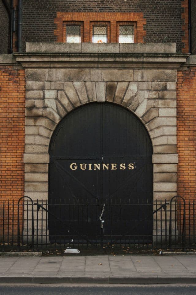 La porte voûtée noire de la brasserie Guinness avec des lettres dorées, encastrée dans une arche en pierre sur un bâtiment en briques rouges.