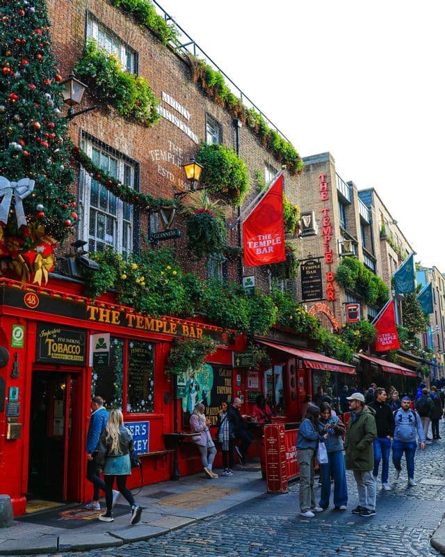 La façade rouge de The Temple Bar sur une rue pavée, décorée d'un sapin de Noël, de guirlandes et de lumières.