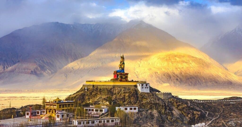 Una grande statua del Buddha seduto su un monastero in cima a una collina si affaccia su una valle con vaste montagne sullo sfondo
