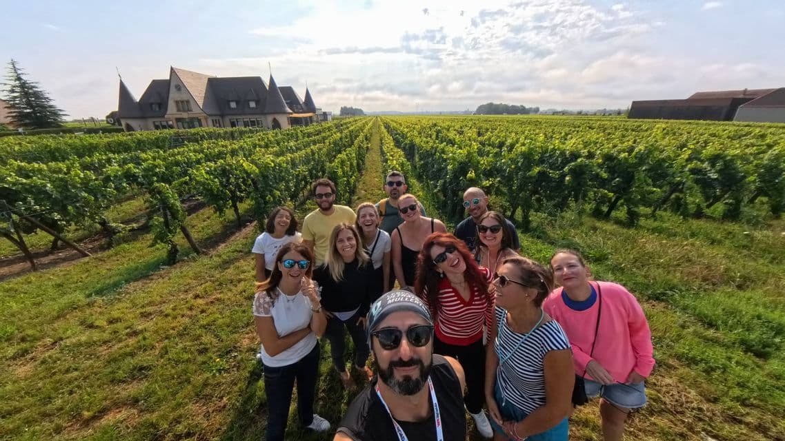Un gruppo WeRoad si scatta un selfie in un grande vigneto con un castello sullo sfondo.