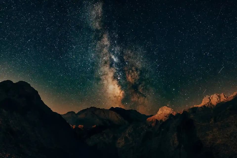 The Milky Way galaxy arches across a star-filled night sky over the dark silhouette of a rugged mountain range.