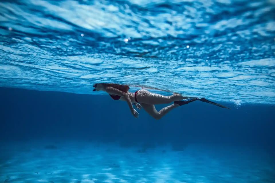 A woman wearing fins and a snorkel mask swims just under the rippled surface of the blue ocean.
