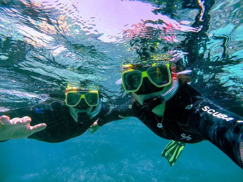 Dos personas de un viaje en grupo de WeRoad haciéndose una selfie bajo el agua mientras practican snorkel en aguas cristalinas.