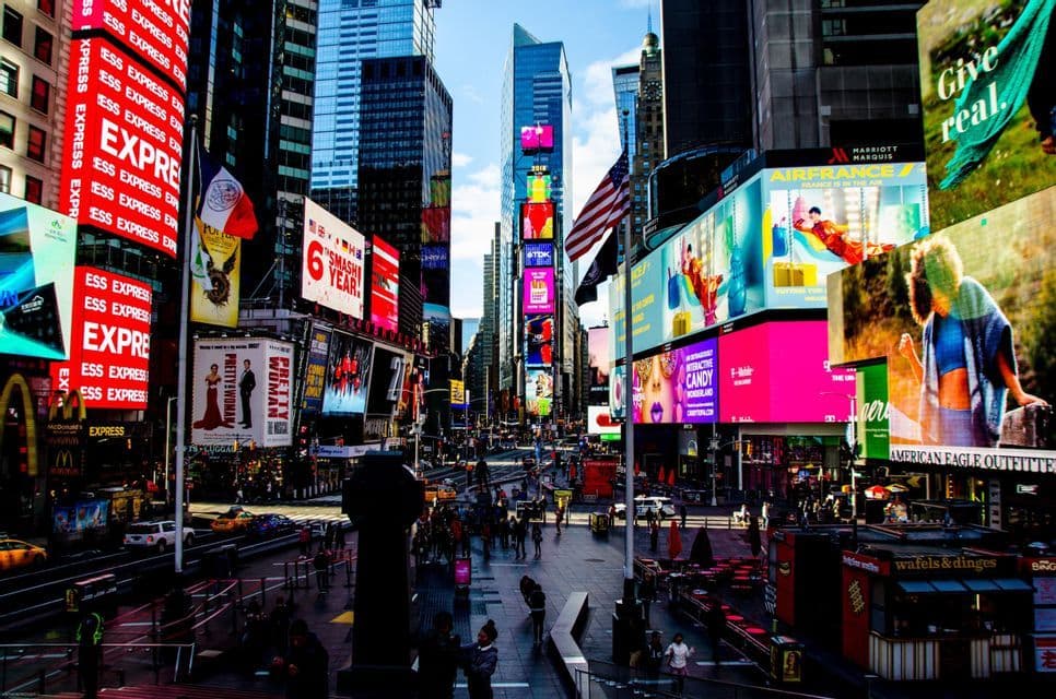 A high-angle view of a bustling city street surrounded by skyscrapers covered in large, vibrant digital advertisements and billboards.