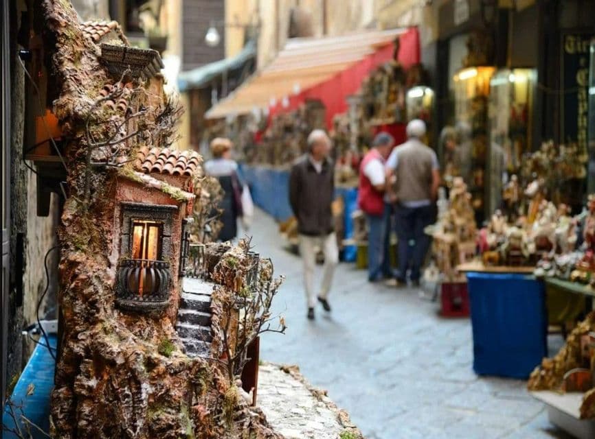 Un modello in miniatura dettagliato di una casa rustica con una finestra illuminata, esposto in un mercato all'aperto, con persone sullo sfondo.