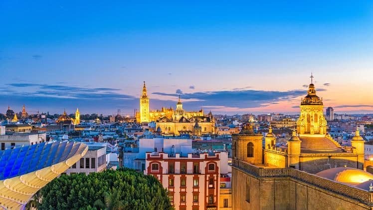 Un paesaggio urbano illuminato con una grande cattedrale ed edifici storici contro un cielo crepuscolare.