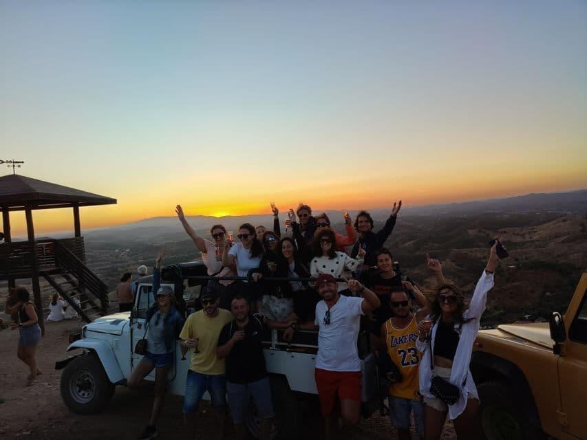 Un viaggio di gruppo WeRoad in festa con un brindisi accanto a un veicolo fuoristrada su una collina panoramica al tramonto.