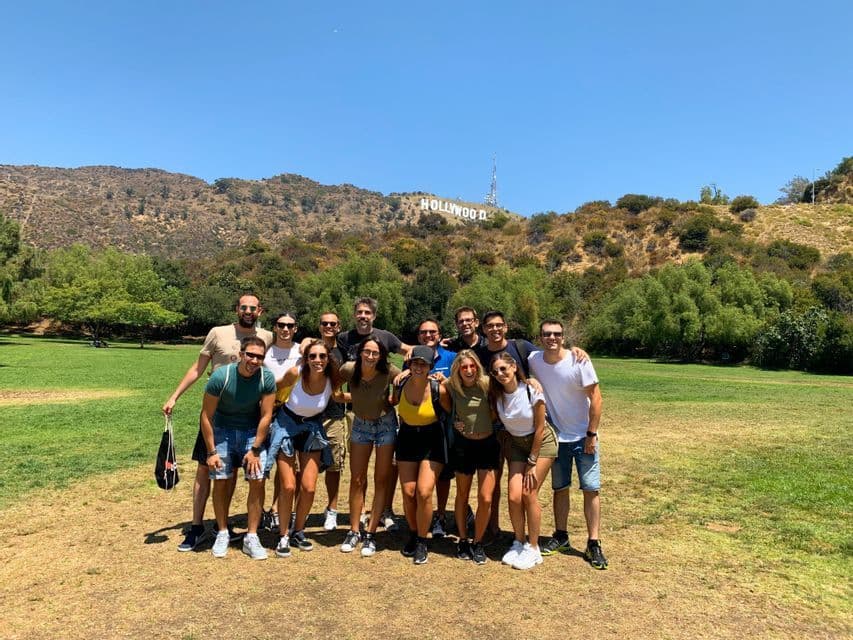 A WeRoad group trip posing together for a photo on a grassy field with the Hollywood sign on a hill in the background.