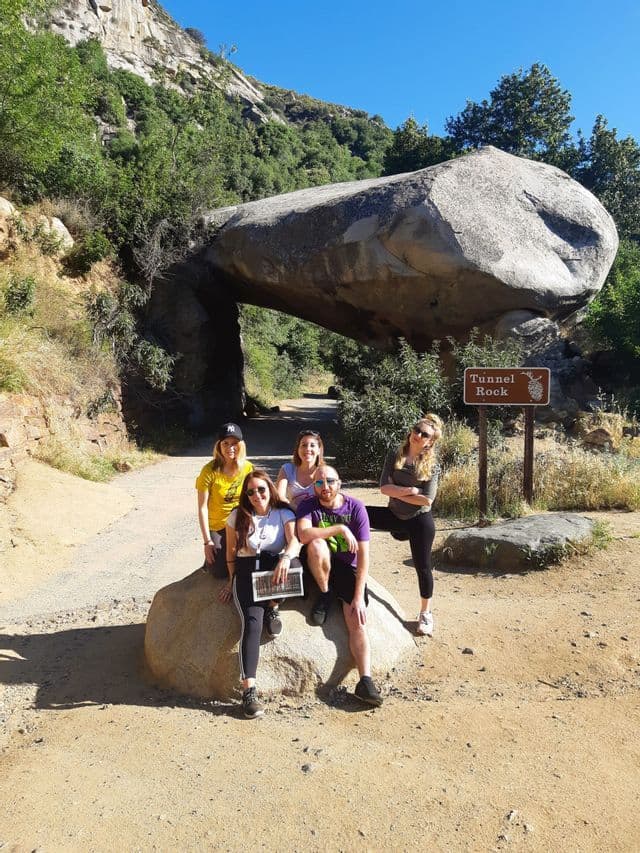 Un voyage de groupe WeRoad de cinq personnes posant pour une photo devant l'impressionnante formation rocheuse Tunnel Rock par une journée ensoleillée.