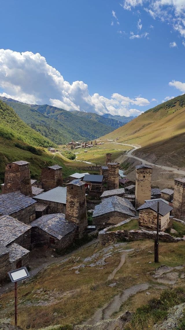 Un gruppo di vecchie case in pietra e torri con tetti in ardesia in una verde valle montana sotto un cielo parzialmente nuvoloso