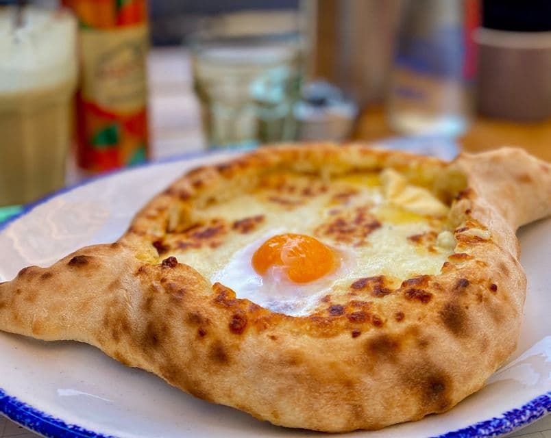 Un khachapuri georgiano, un pane a forma di barca ripieno di formaggio fuso e condito con un tuorlo d'uovo crudo, su un piatto.