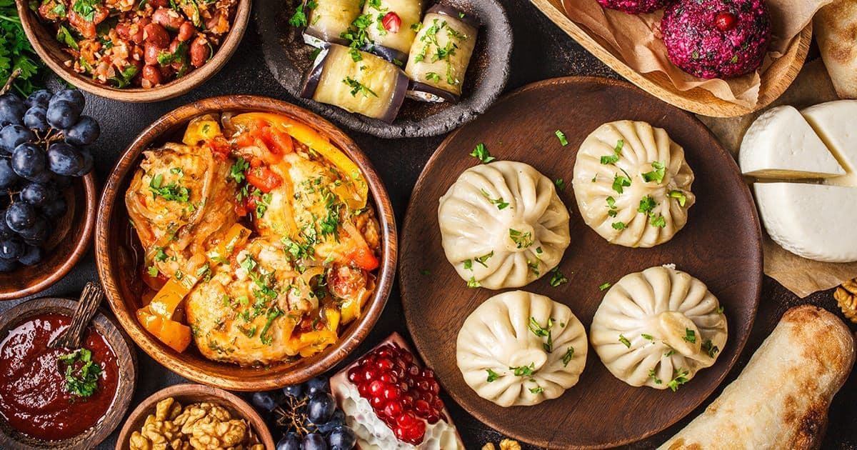 Una panoramica dall'alto di una tavolata di cibo tradizionale georgiano con khinkali, stufato, formaggio e involtini di melanzane.