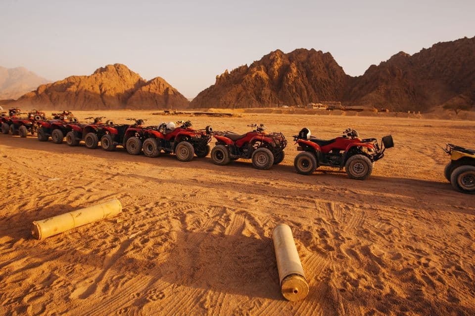 Une longue file de quads rouges stationnés dans le désert avec des montagnes rocheuses en arrière-plan au coucher du soleil.