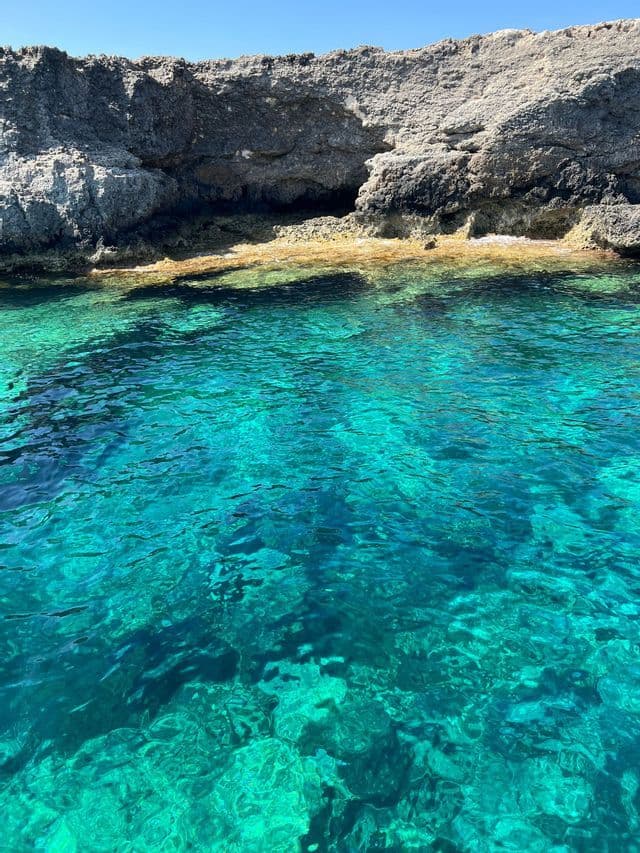 L'acqua limpida e turchese rivela il fondale roccioso ai piedi di una scogliera impervia in una giornata di sole.