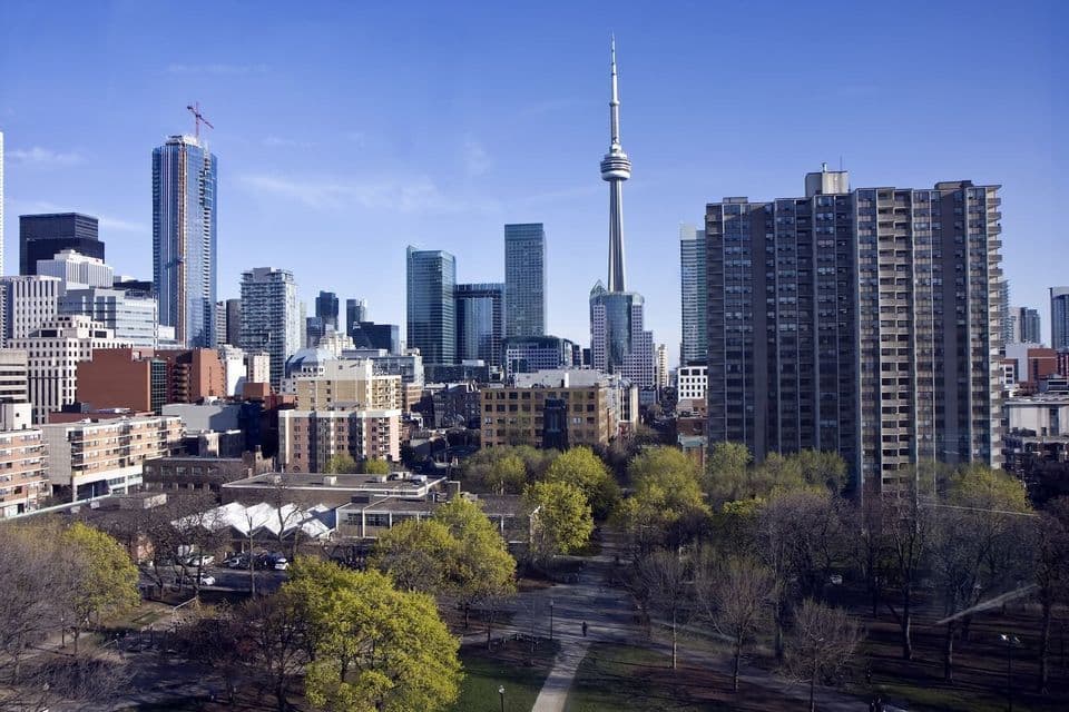 A sprawling city skyline with a prominent needle tower and skyscrapers, seen over a green park under a clear blue sky.