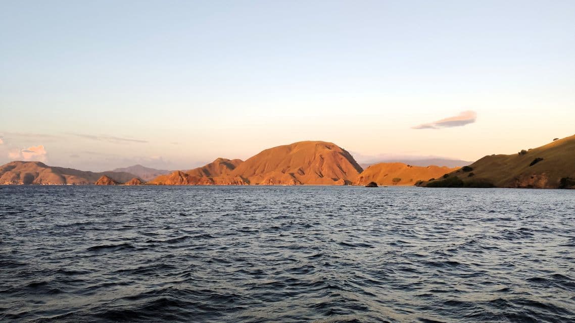 Goldenes Licht der untergehenden Sonne erhellt eine Kette karger, sanfter Hügel am tiefblauen Meer.