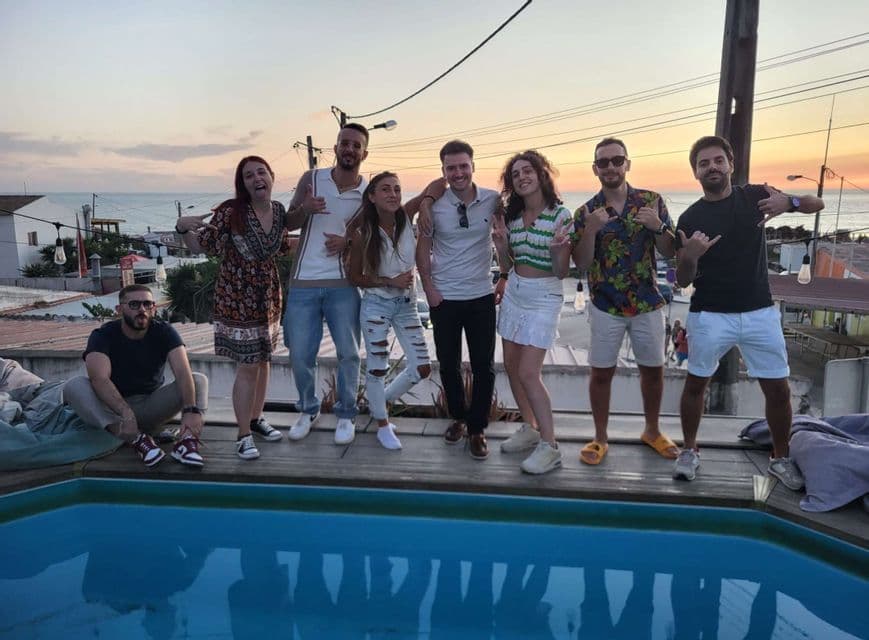 Un viaggio di gruppo WeRoad in posa insieme su una terrazza panoramica con piscina al tramonto e il mare sullo sfondo.