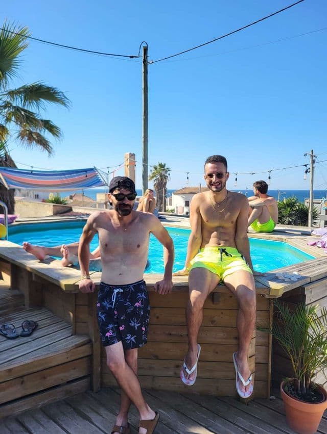 Due uomini in costume da bagno di un viaggio di gruppo WeRoad in posa a bordo piscina in una giornata di sole.