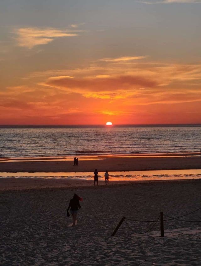 Un viaggio di gruppo WeRoad ammira il tramonto sull'oceano da una spiaggia sabbiosa sotto un cielo arancione.