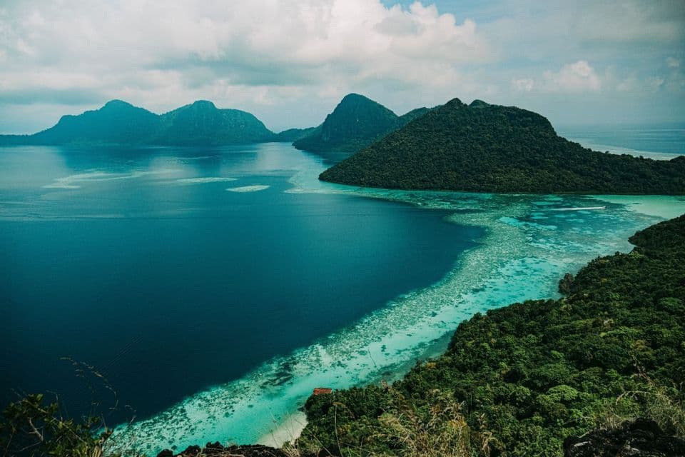 Vista aérea de exuberantes islas tropicales verdes rodeadas de aguas azul profundo y turquesa con un arrecife de coral visible.