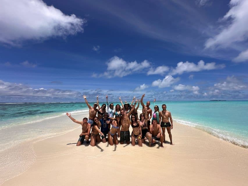 Un viaje en grupo de WeRoad posando juntos en un banco de arena blanca rodeado de agua turquesa bajo un cielo azul con nubes.