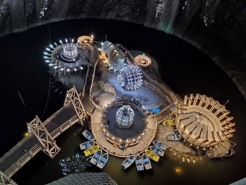 Un parco divertimenti illuminato costruito su un'isola di legno all'interno di una vasta caverna sotterranea con un lago e barche a remi.