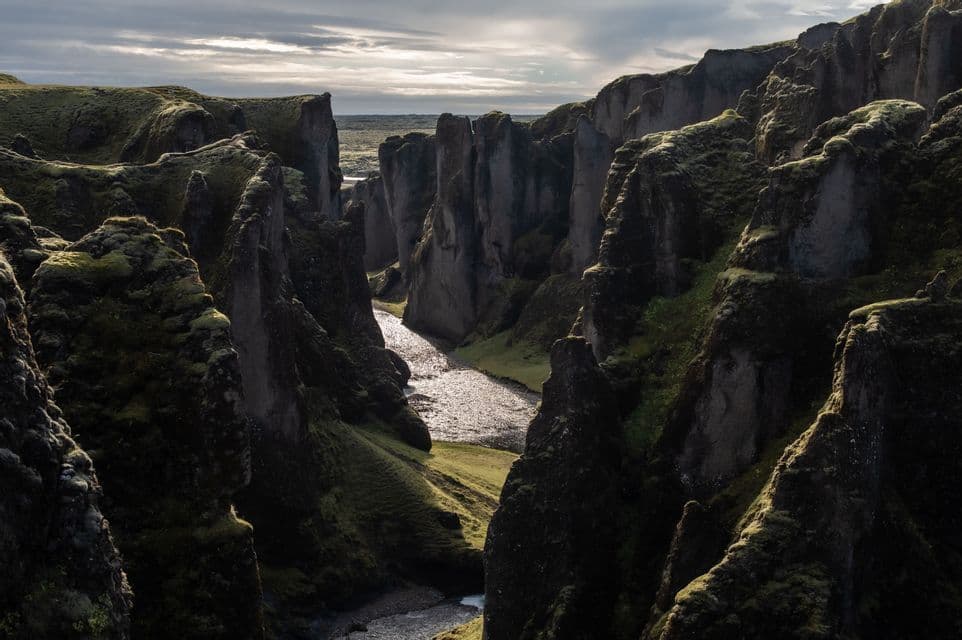Un río sinuoso refleja la luz del sol mientras fluye por un cañón profundo con formaciones rocosas empinadas y cubiertas de musgo.
