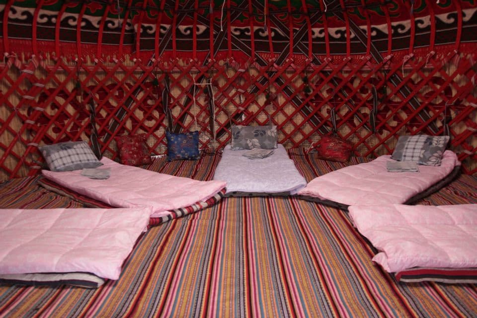 L'intérieur d'une yourte traditionnelle avec plusieurs lits disposés en cercle sur un sol rayé coloré.