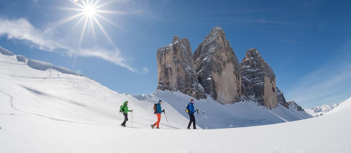 Tres personas de un viaje en grupo de WeRoad con raquetas de nieve en un paisaje montañoso nevado bajo un cielo despejado y soleado.