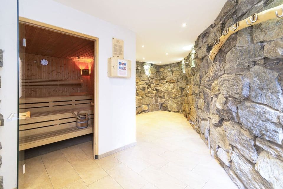 Un interior de spa moderno que muestra una sauna de madera con puerta de cristal que conduce a un pasillo con una pared de piedra rugosa.