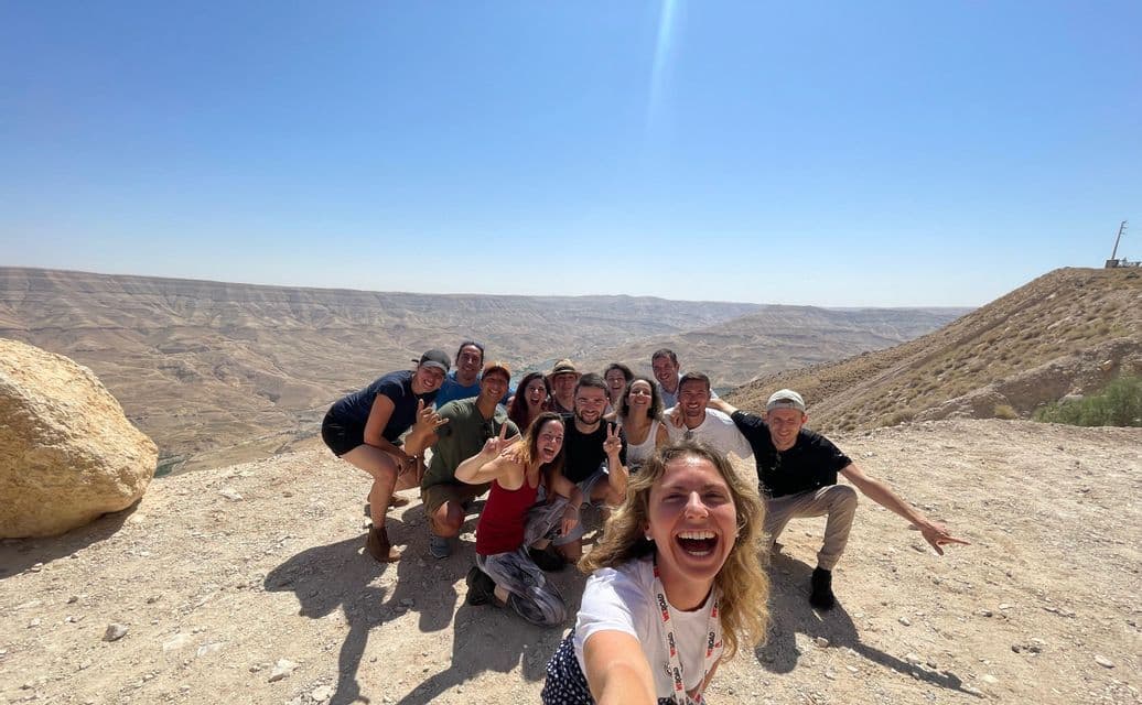 Un groupe WeRoad prend un selfie sur une colline ensoleillée, avec un vaste paysage de canyon aride en arrière-plan.