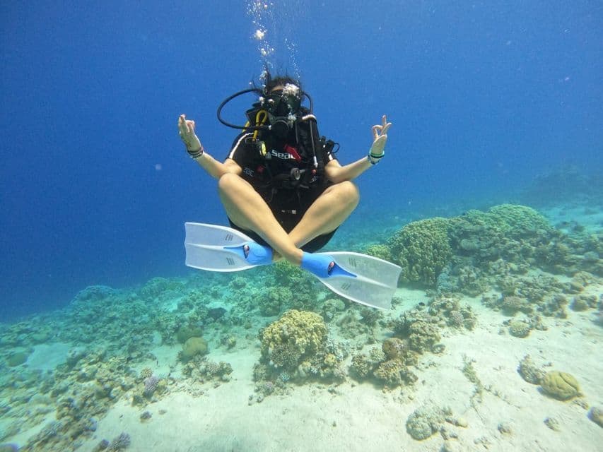 Un plongeur sous-marin médite en position du lotus, flottant sous l'eau au-dessus d'un fond sableux avec des récifs coralliens.