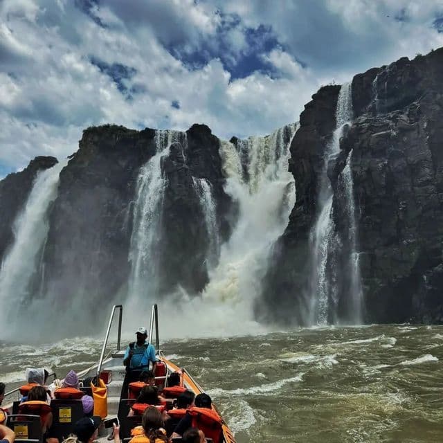 Un viaje en grupo de WeRoad en barco avanza sobre aguas agitadas hacia una enorme cascada que se precipita por un acantilado rocoso.
