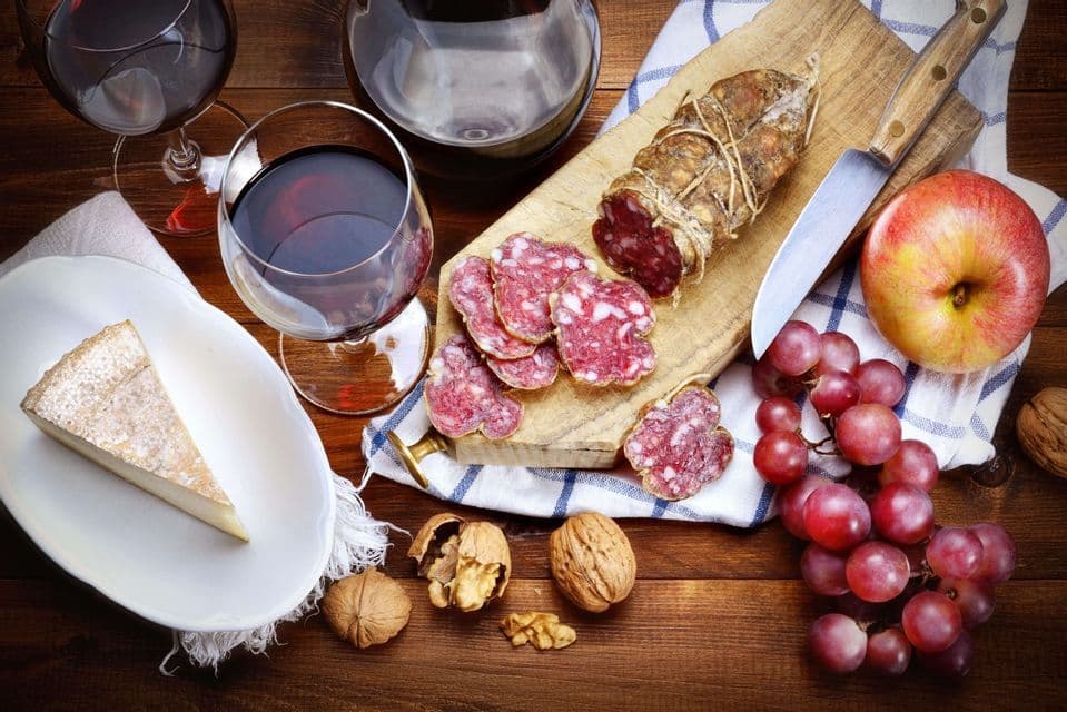 Una composizione di vino rosso, salame affettato, formaggio, uva, una mela e noci su un tavolo di legno.